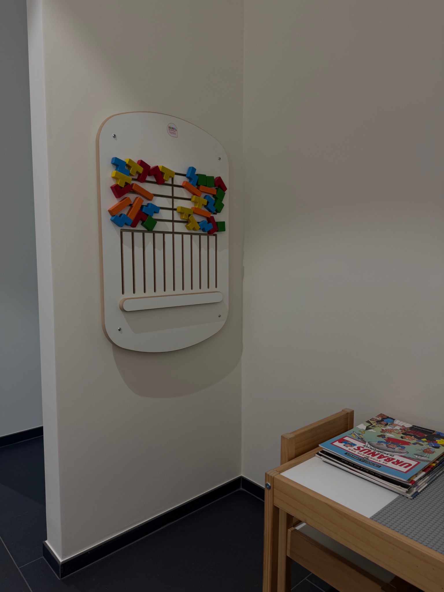 Speelhoek met activiteitenbord en kinderboeken bij Petillion Optiek